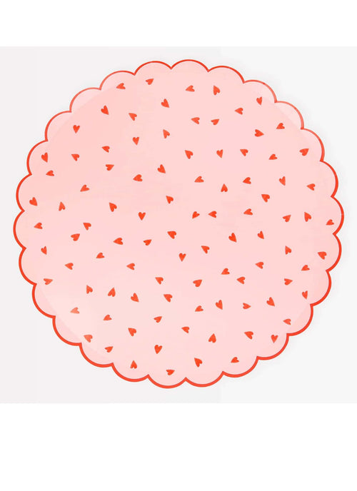 A round pink dinner plate with a red heart pattern and scalloped border.