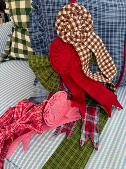 A collection of handmade fabric rosettes and ribbons made from plaid and gingham shirts, displayed on a blue and white striped couch cushion.