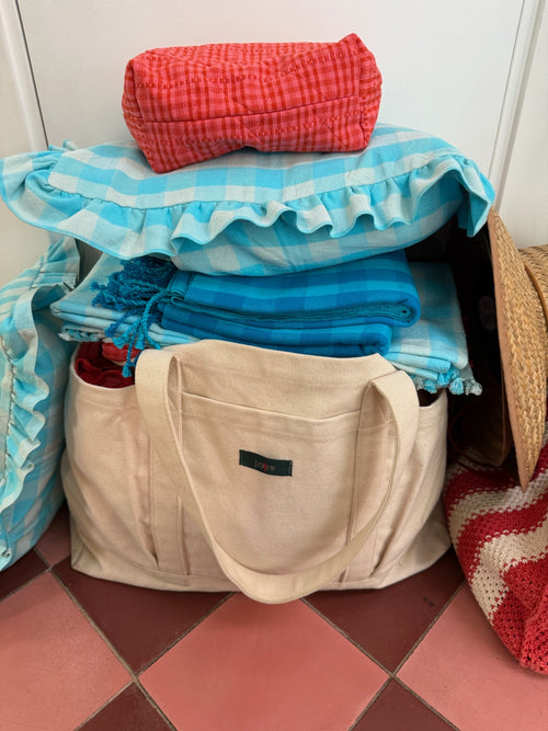 Stack of folded clothes and a beige bag on a tiled floor against a white wall.