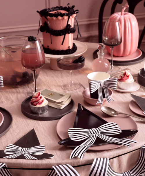 Decorative table setting with black and white bow accents, pink cake, and wine glasses.