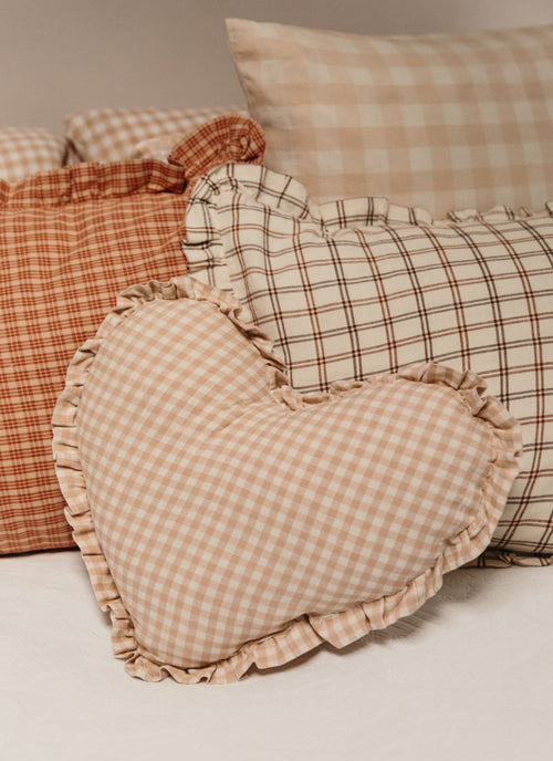 Heart-shaped checkered pillow with other patterned pillows on a neutral background