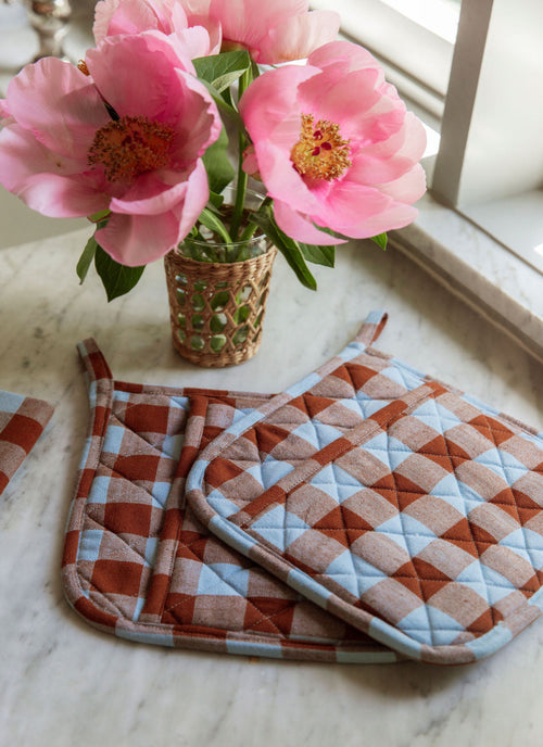Checkered pot holders on a marble surface with pink flowers in the background