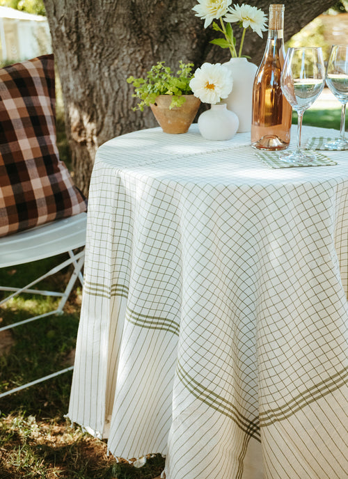 Outdoor setting with a tablecloth, wine bottle, and glasses near a tree.