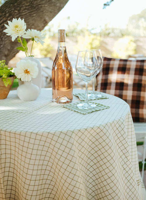 Bottle of rosé wine with two glasses on a checkered tablecloth outdoors.