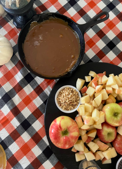 Cast iron skillet with apple pie filling on a checkered tablecloth with apples and nuts.