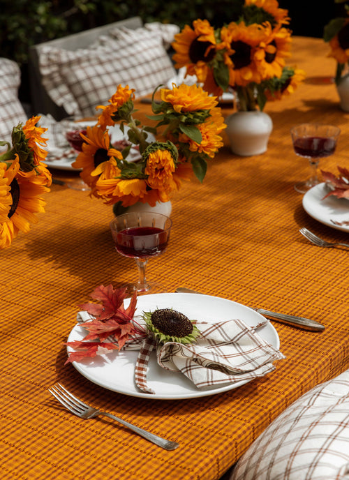 Decorative table setting with sunflowers, wine glasses, and fall-themed place settings on an orange tablecloth.