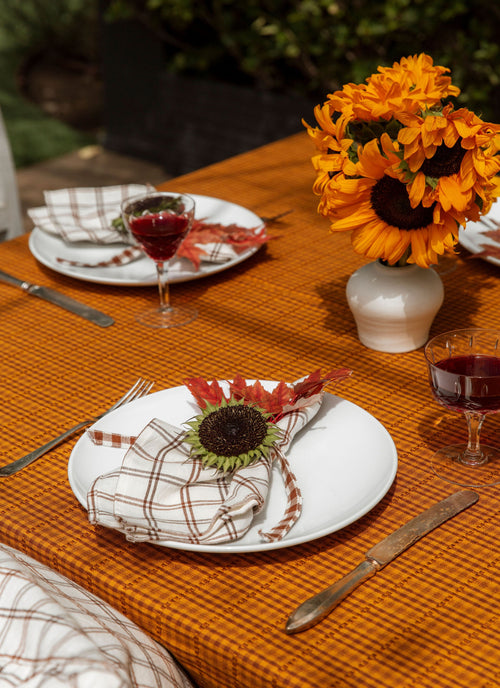 Dining table set with plates, napkins, and a vase of sunflowers on an orange tablecloth.