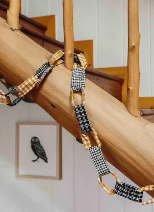 A decorative garland made of black and gold patterned fabric links, displayed strung along a wooden beam.