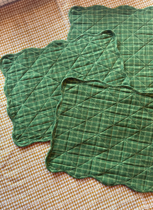 Two green quilted placemats on a checkered tablecloth