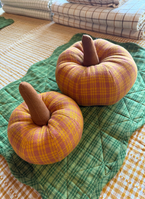 Two checkered pumpkins on a green quilt with a plaid fabric background
