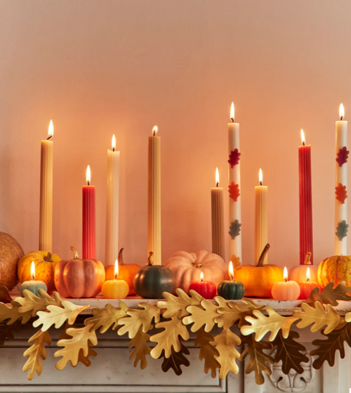 Decorative autumn mantel with candles, pumpkins, and leaf garland.