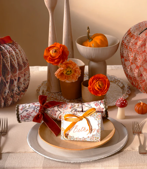 Decorative table setting with pumpkins, flowers, and a card on a checkered tablecloth.