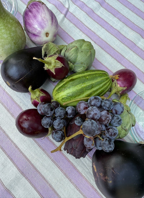 Assorted vegetables including eggplants, zucchini, and grapes on a striped fabric background