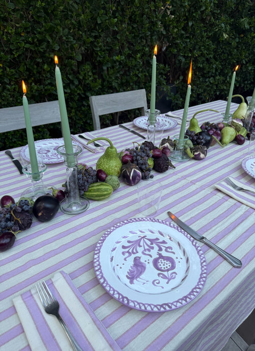 Outdoor table setting with purple and white striped tablecloth, candles, and decorative plates.
