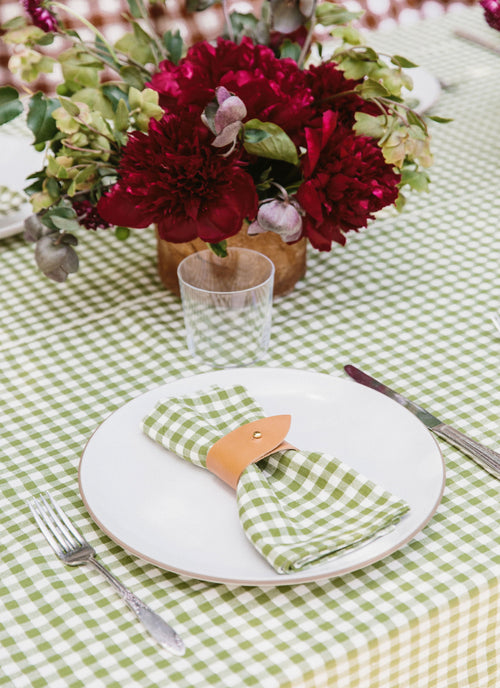 Table setting with red flowers, green checkered tablecloth, and white plate.