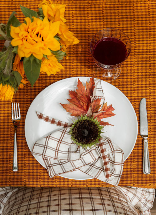 Autumn-themed table setting with leaves, sunflowers, and a glass of red wine on an orange checkered tablecloth.