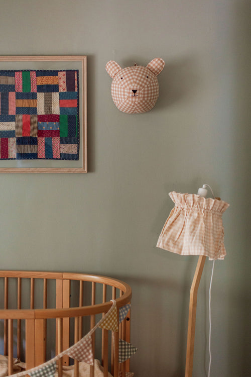 Nursery room with wooden crib, checkered lamp, and patchwork art on a green wall.