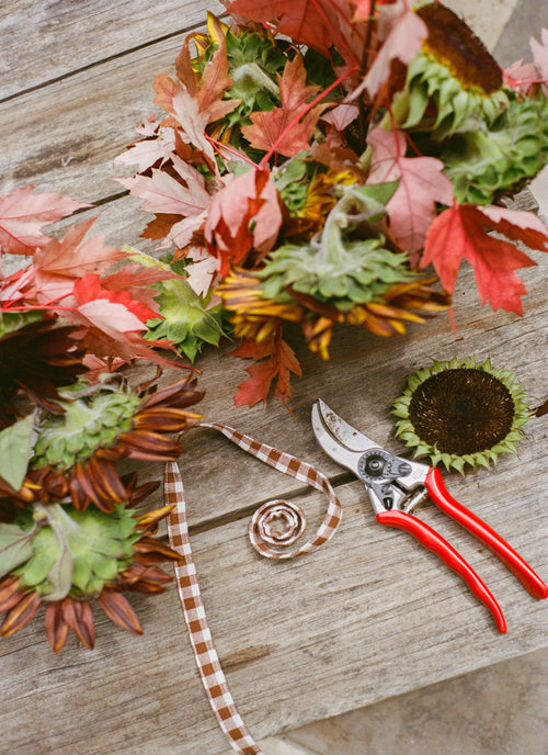 Bouquet of autumn leaves and sunflowers with red-handled pruning shears on a wooden surface.