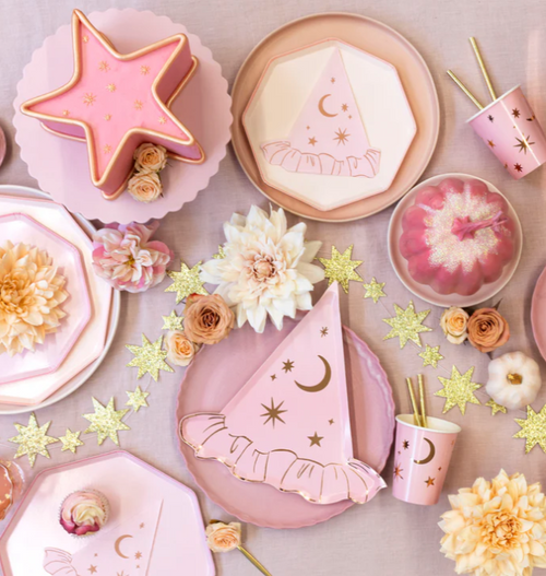 Pink party supplies including plates, cups, and a cake with floral decorations on a light background.