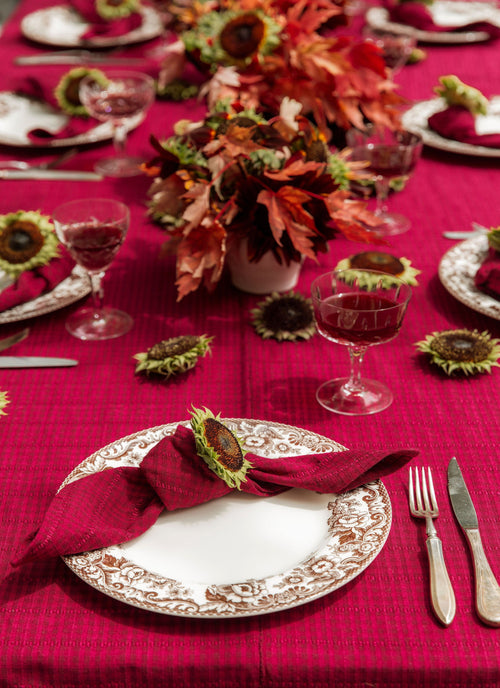 Decorative table setting with red tablecloth, sunflower centerpieces, and elegant cutlery.