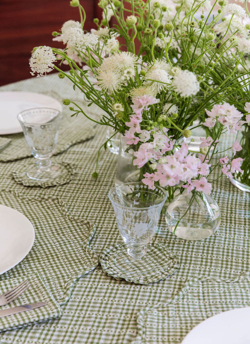 Table setting with floral arrangements and glassware on a checkered tablecloth.