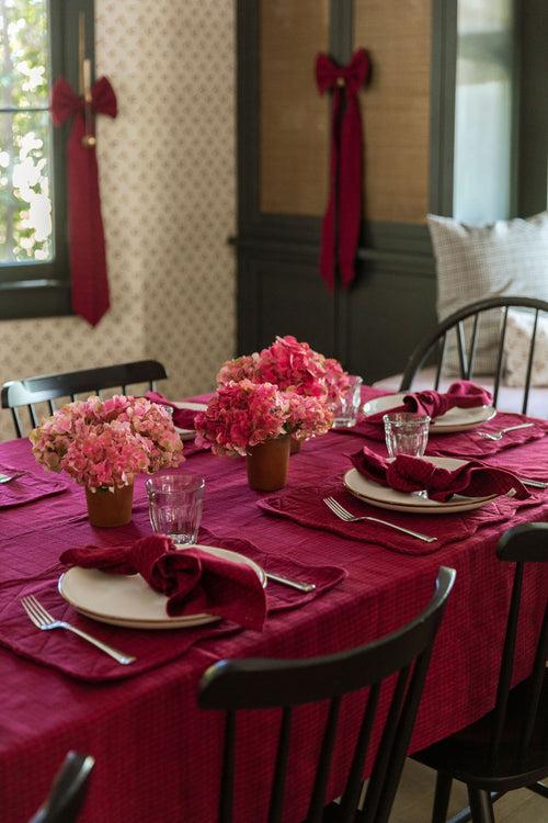 Dining table set with Purple tablecloth, flowers, and place settings in a room with decorative ribbons on windows.