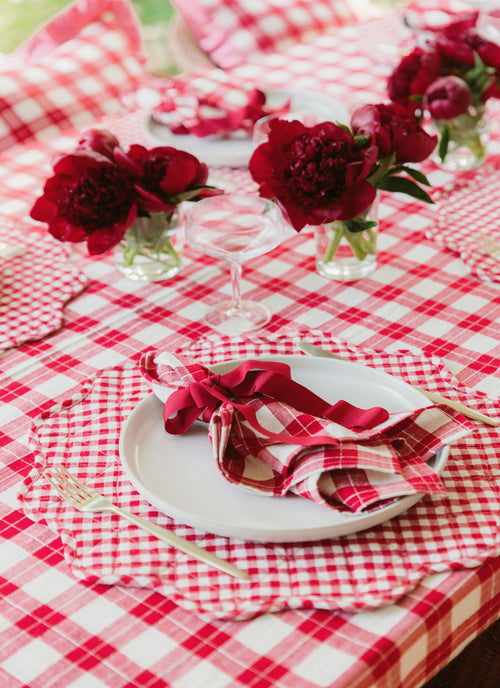Table setting with red flowers, checkered tablecloth, and white plates.