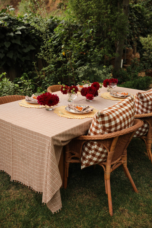 Outdoor table setting with red flowers and checkered tablecloth in a garden.