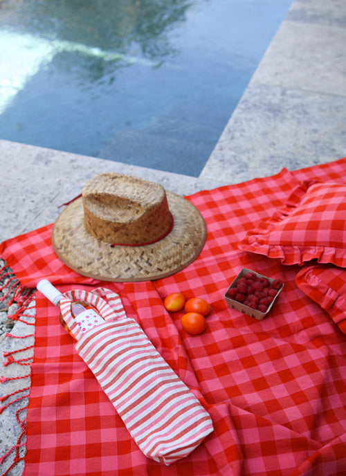 A red and white striped wine tote bag on a red checkered picnic blanket, with a straw hat and some tomatoes in the background.