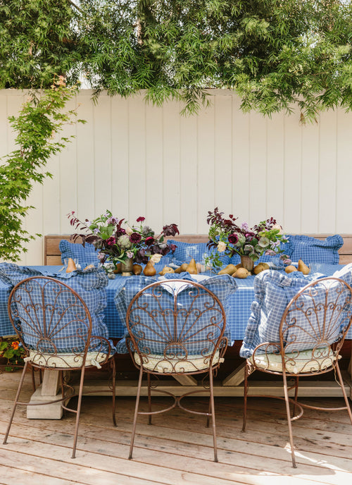 Outdoor dining setup with a tablecloth, chairs, and floral arrangements.